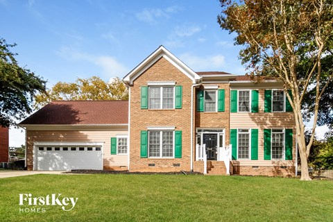 a brick house with green shutters and green garage doors