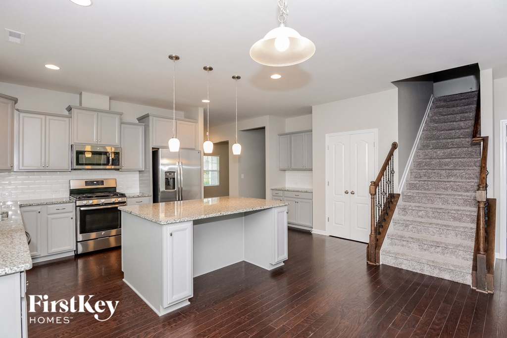 a white kitchen with a marble counter top and a staircase