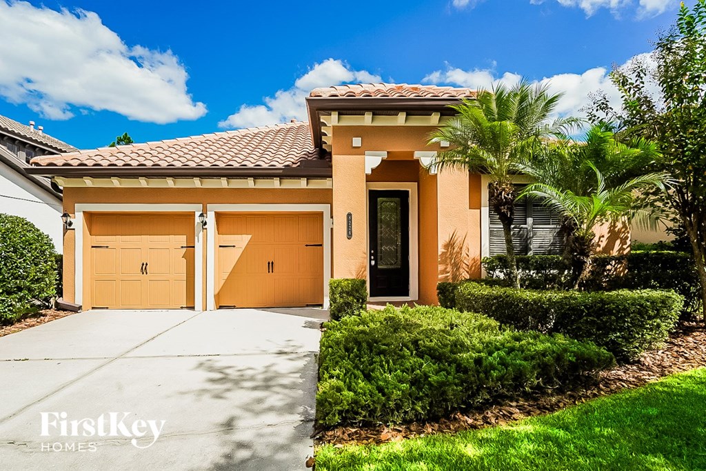 A house with a brown roof and tan garage doors is for sale.