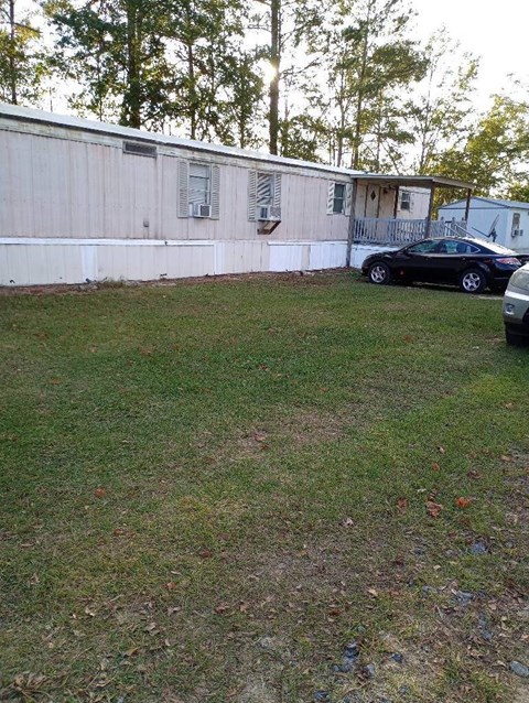 A black car is parked in a yard next to a white building.