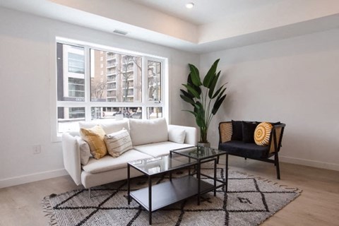 A living room with a white couch, a glass coffee table, and a black chair with a yellow pillow.