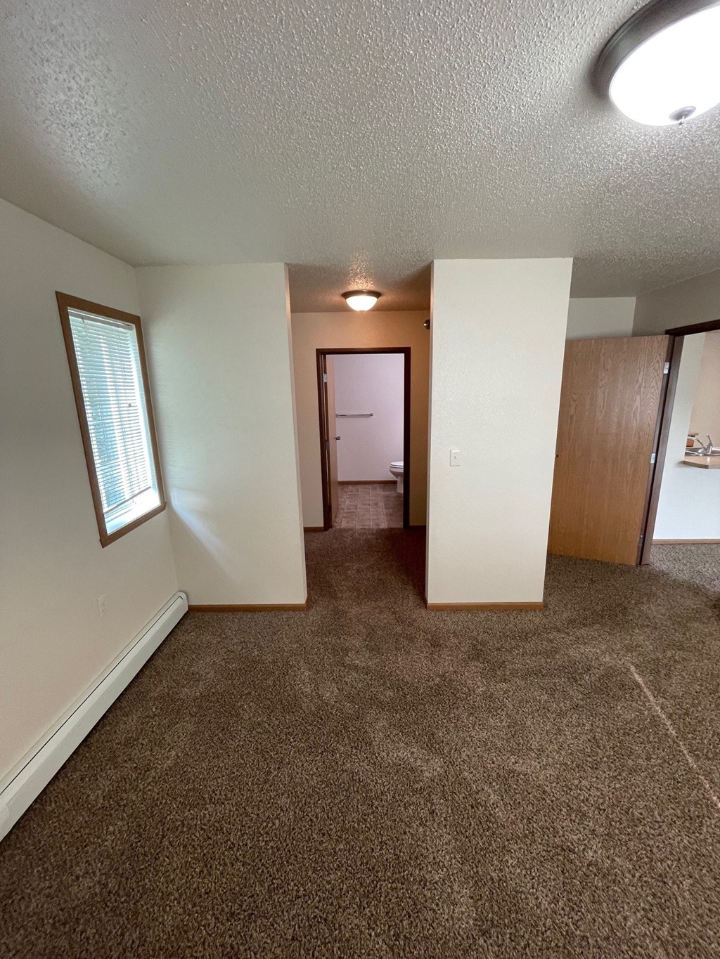 an empty living room with carpeting and a hallway with a door to a bedroom