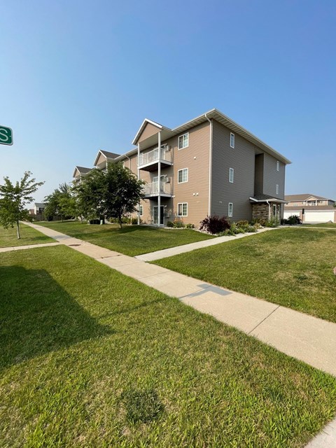 a sidewalk leading to an apartment building on a green lawn