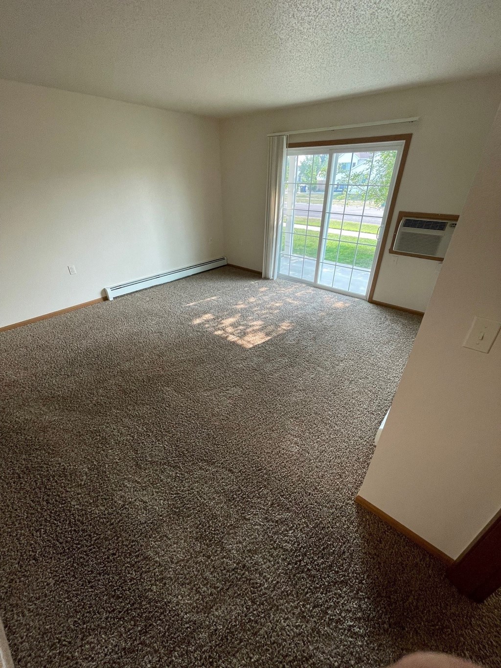 an empty living room with carpet and a sliding glass door