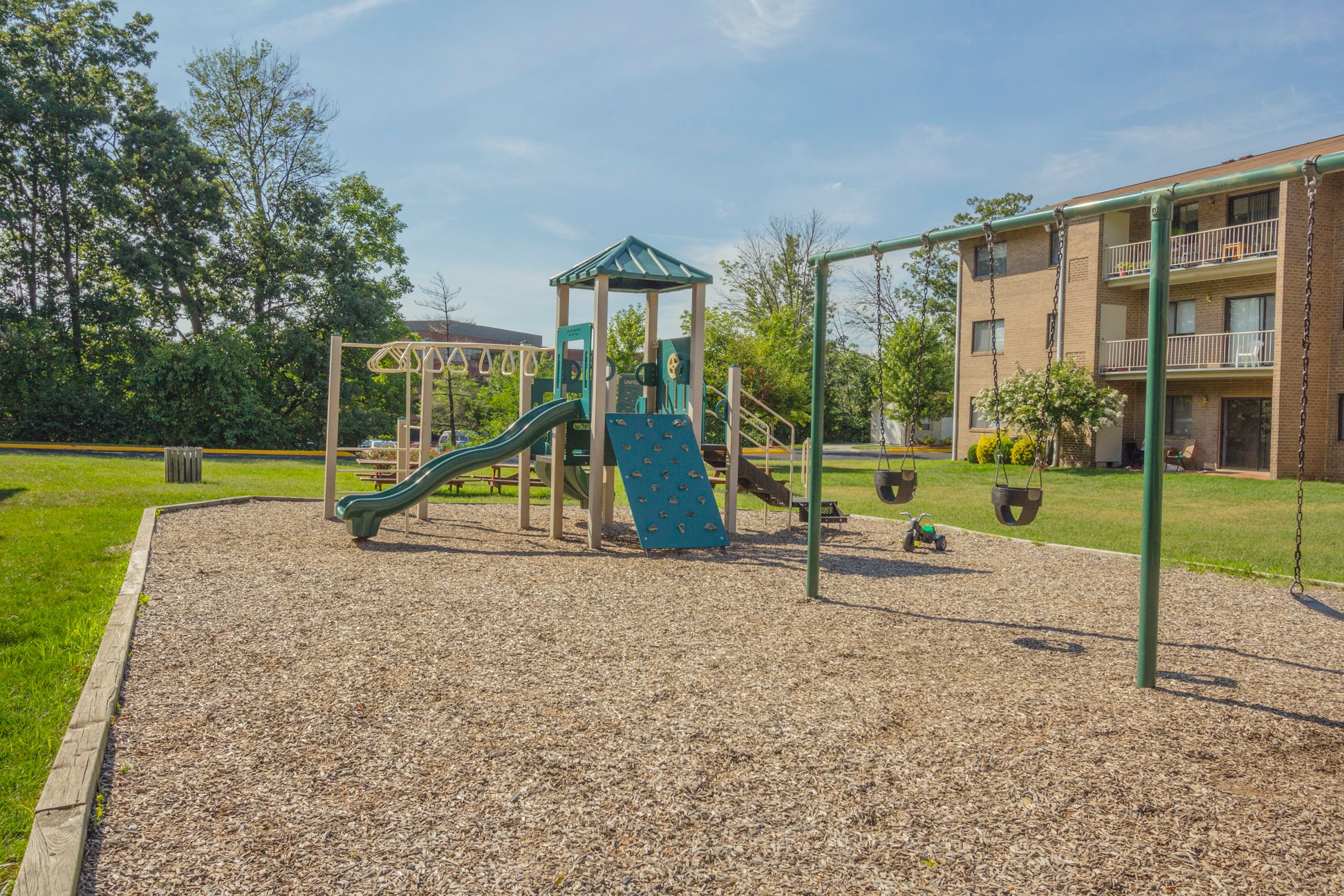 A playground with a green slide and a wooden swing set.
