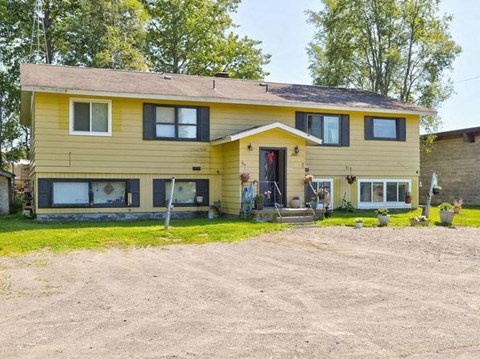 a yellow house with a yard and a gravel driveway