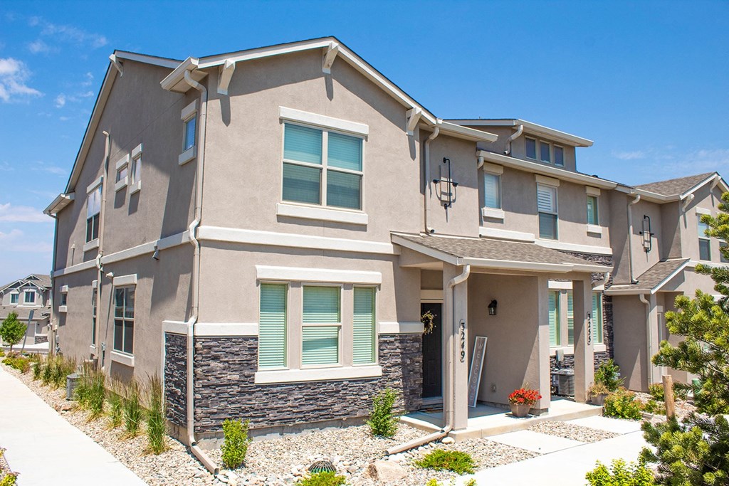 a tan house with green shutters and a sidewalk