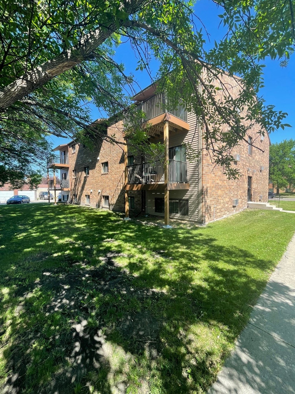 a brick apartment building with a green lawn and a tree