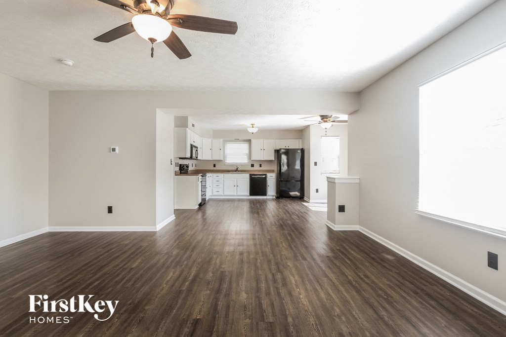 an empty living room and kitchen with wood floors and a ceiling fan