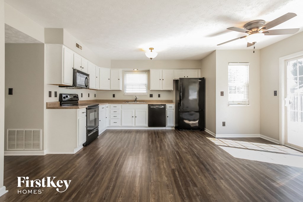 an empty kitchen with white cabinets and a black refrigerator