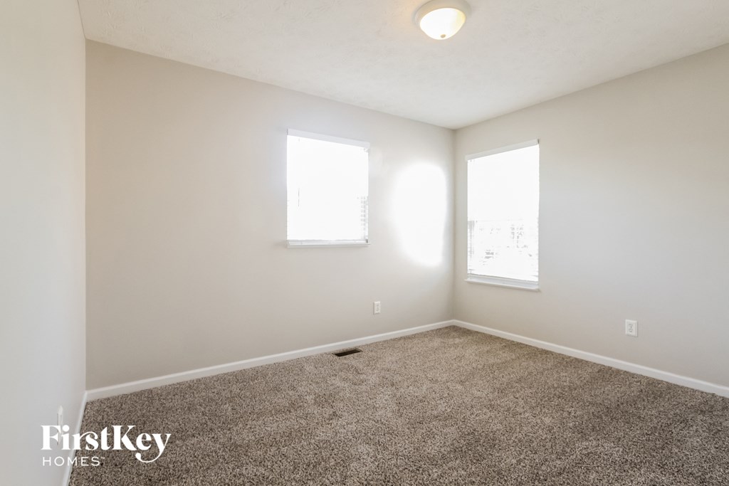 an empty room with carpet and two windows