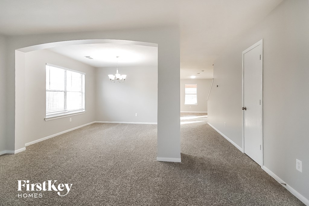 A spacious, empty room with a carpeted floor and a chandelier hanging from the ceiling.