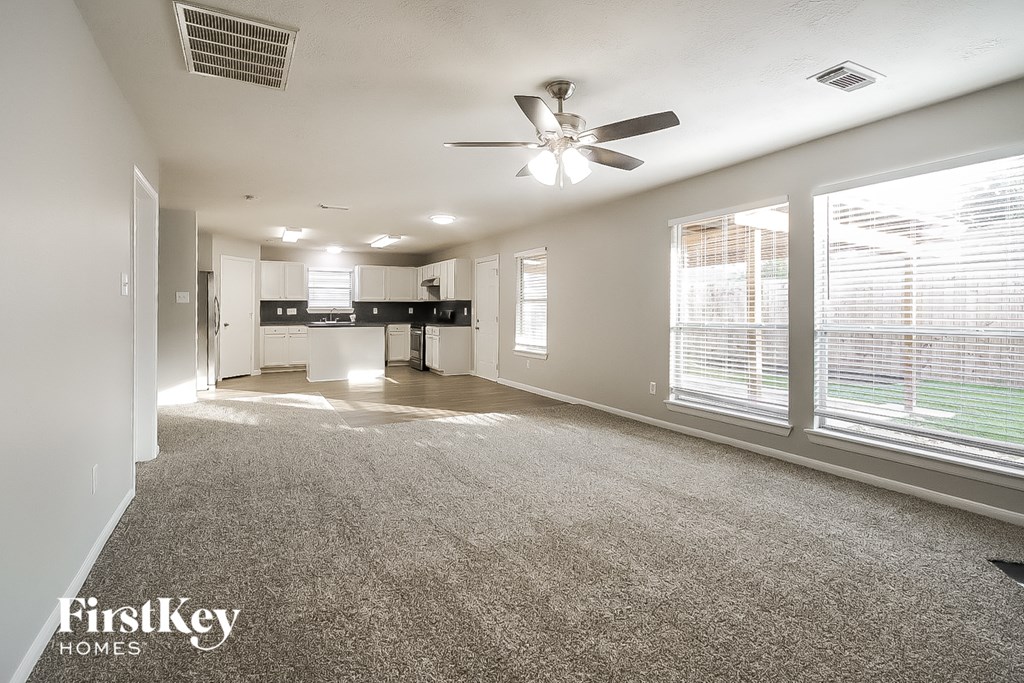 A spacious living room with a ceiling fan and large windows.