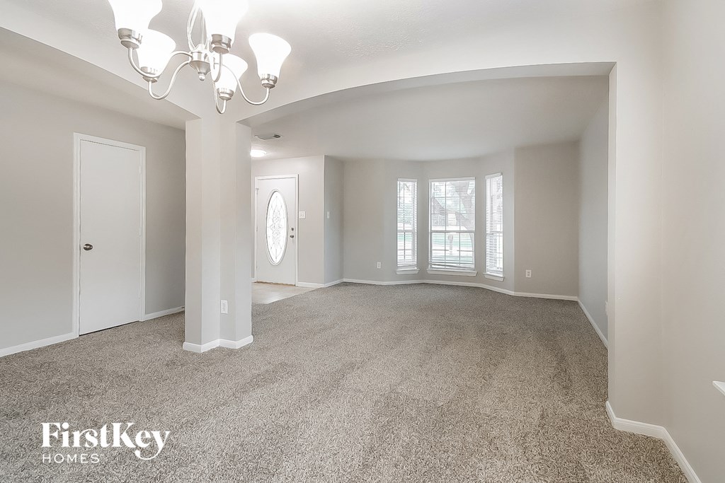 A spacious room with a chandelier and a carpeted floor.