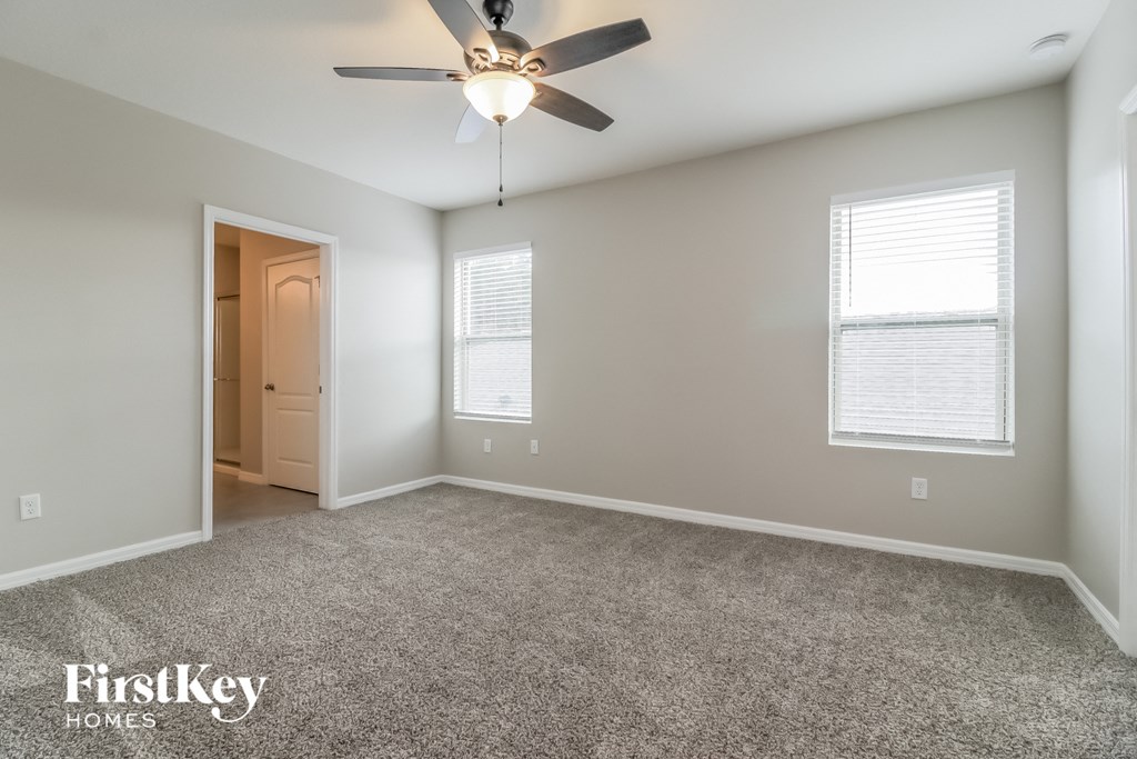 A spacious room with a ceiling fan and two windows.
