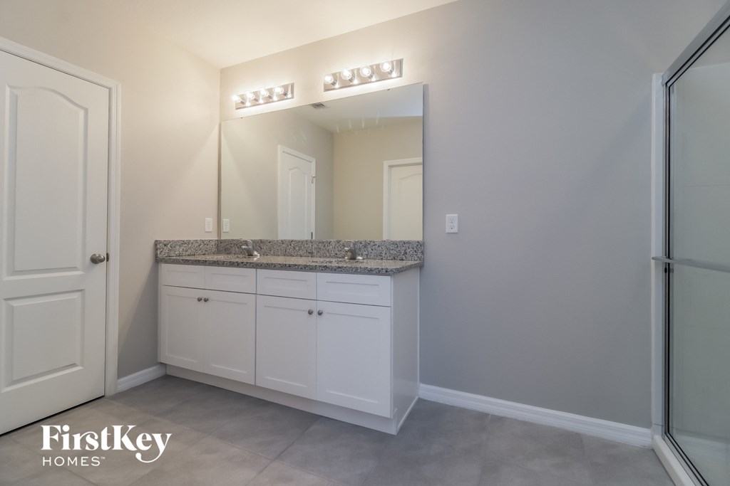 A bathroom with a mirror, sink, and cabinets.