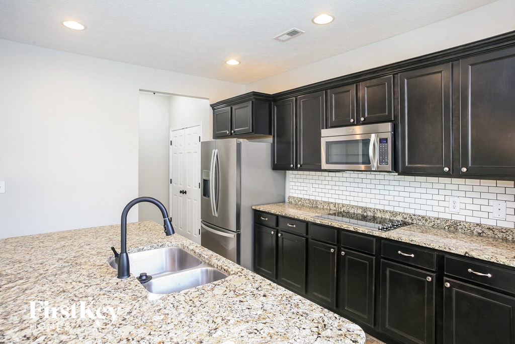 a kitchen with black cabinets and granite counter tops and stainless steel appliances