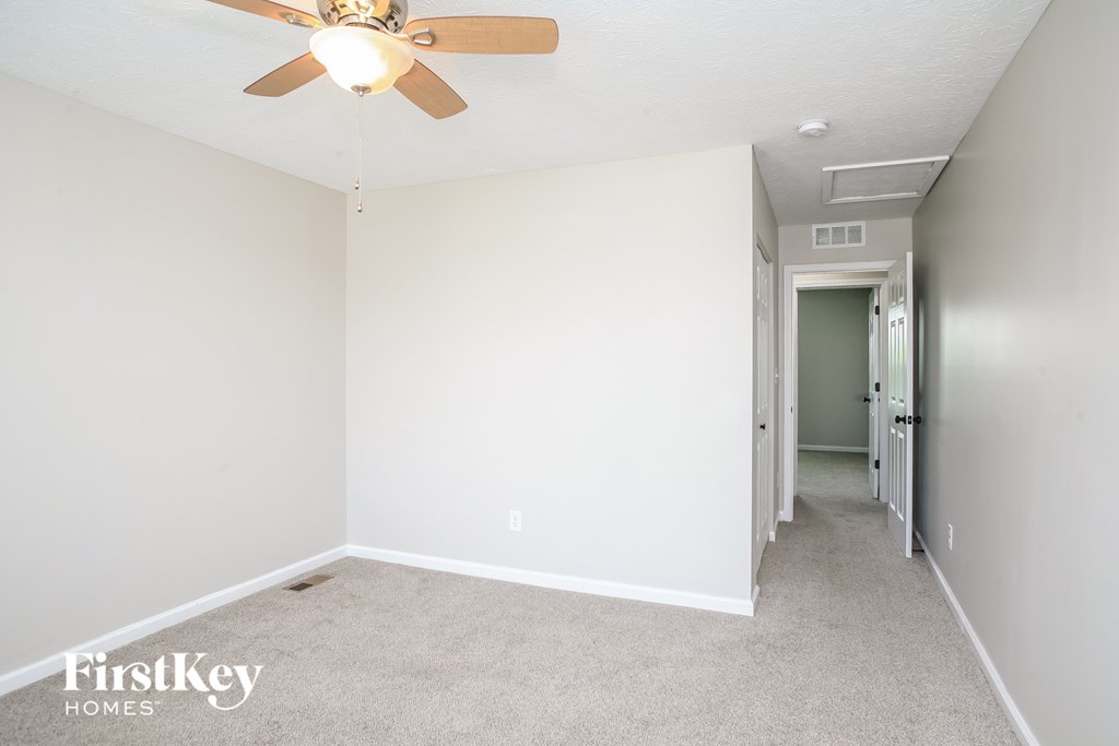 a bedroom with white walls and a ceiling fan     and a hallway