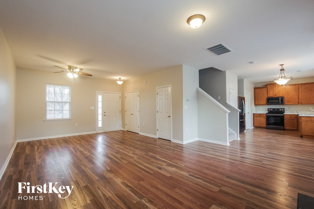 an empty living room with wood flooring and a kitchen
