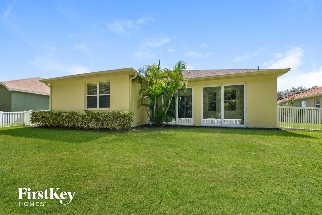 A yellow house with a white fence and a green lawn in front.