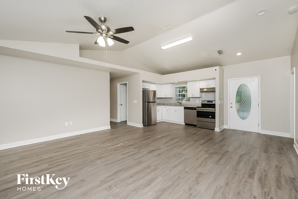 an empty living room with a ceiling fan and a kitchen