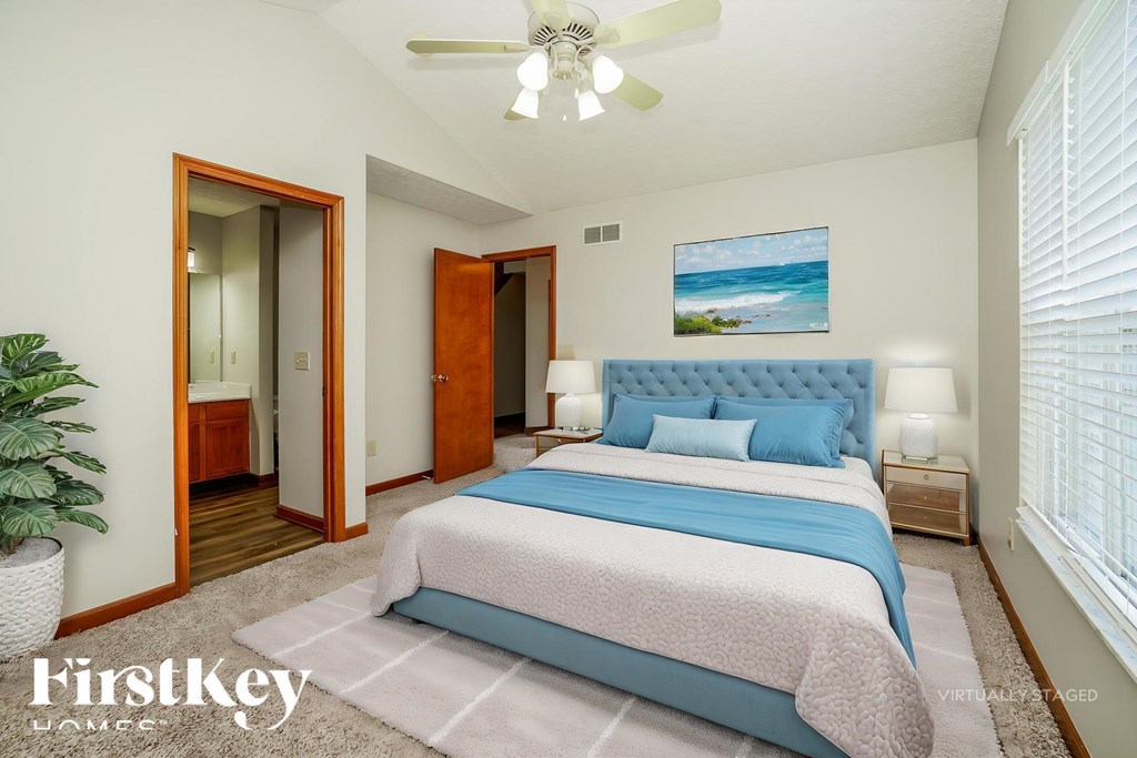 A bedroom with a bed, a ceiling fan, and a painting of a beach scene on the wall.