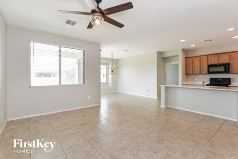 A spacious living room with a ceiling fan and a kitchenette in the background.