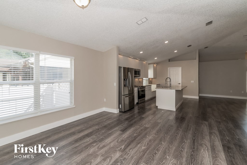 the living room and kitchen of an apartment with wood flooring and a large window