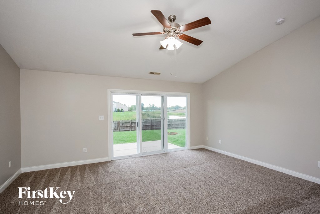 A spacious room with a ceiling fan and sliding glass doors leading to a backyard.