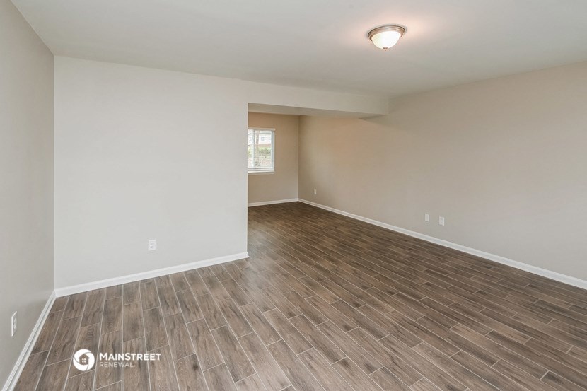 the spacious living room with wood flooring and white walls