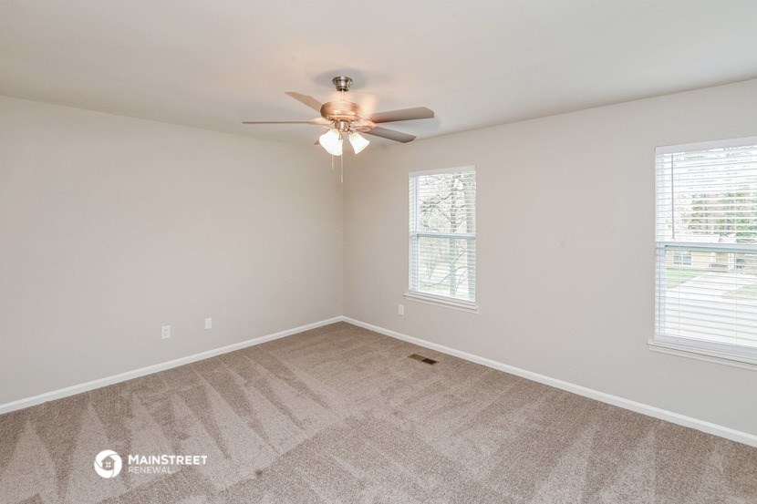 the spacious living room with ceiling fan and carpeting