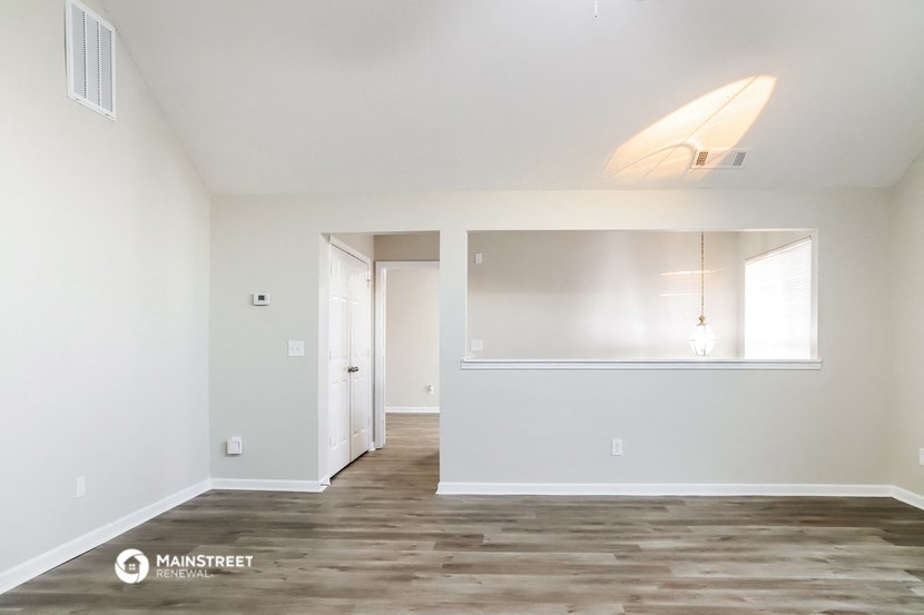 the living room and dining room of an apartment with white walls and wood floors