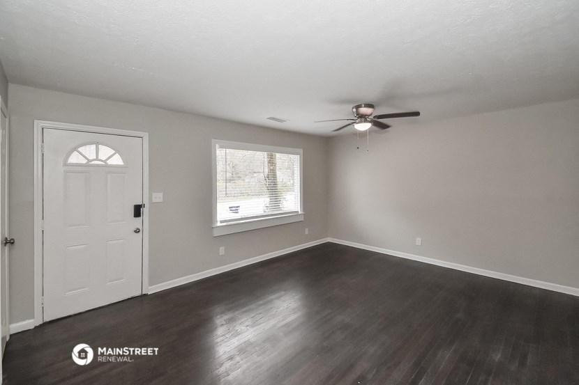 the living room of a house with a white door and a ceiling fan