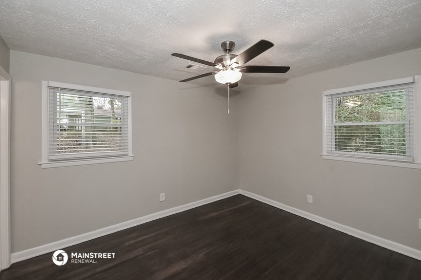 the bedroom of a house with a ceiling fan and two windows