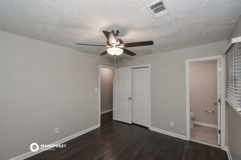 the living room of an apartment with a ceiling fan and a door to the bathroom
