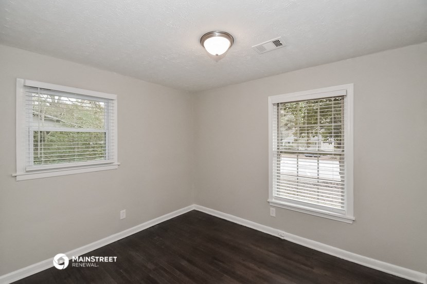 the interior of an empty room with wood flooring and two windows
