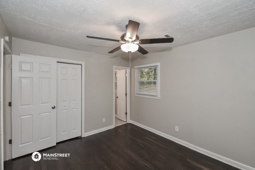 the living room of an apartment with a ceiling fan and a door to the closet