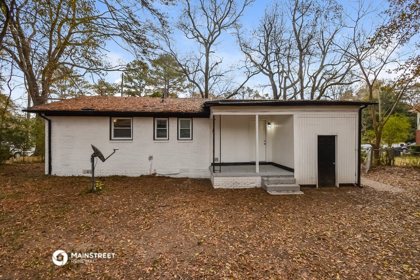 a small white house with a garage in the woods