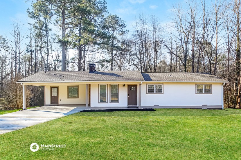 the front of a white house with a lawn and trees