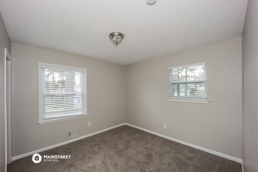 the spacious bedroom with carpeted flooring and two windows