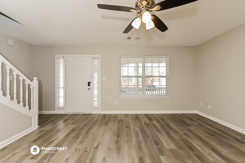 an empty living room with a ceiling fan and a door