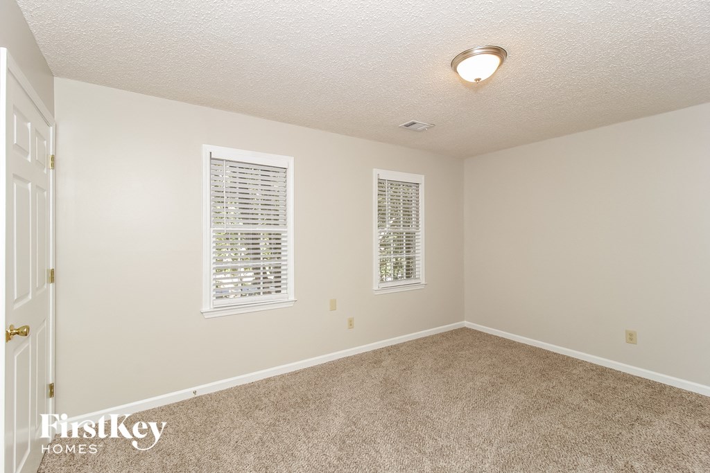 a spacious living room with carpet and two windows