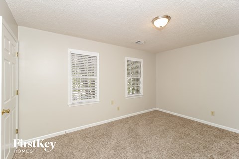 a spacious living room with carpet and two windows