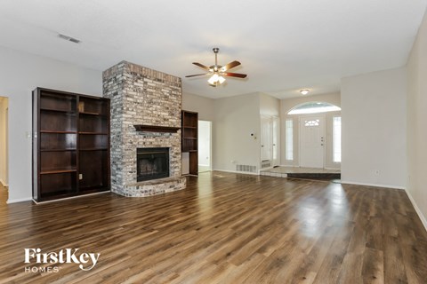 an empty living room with a stone fireplace and wooden floors