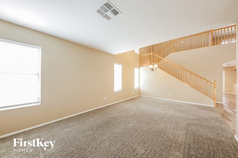 A spacious room with a carpeted floor and a staircase with a wooden railing.