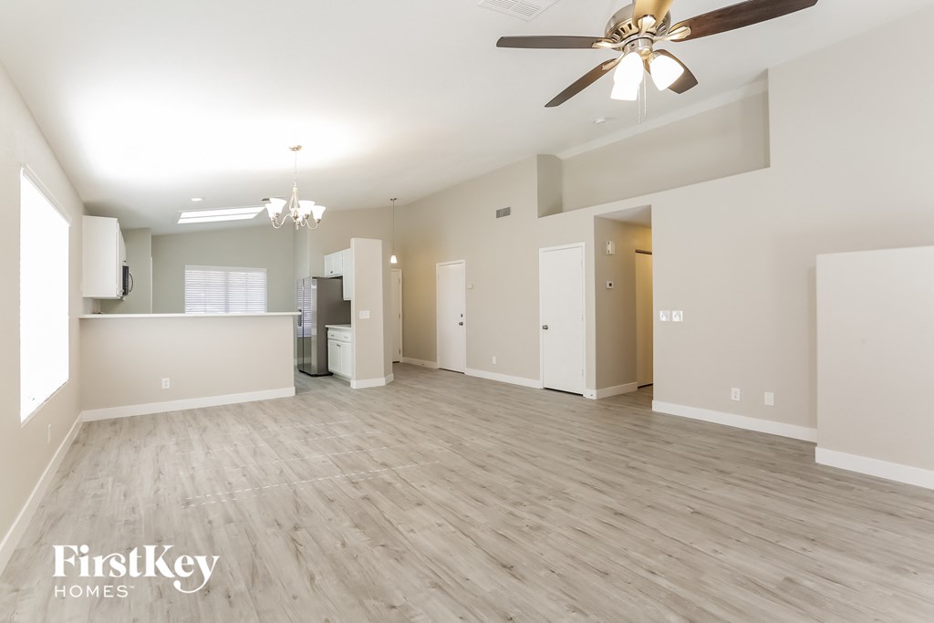 an empty living room with a ceiling fan and a kitchen