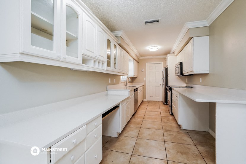a long kitchen with white cabinets and counters and tile floors