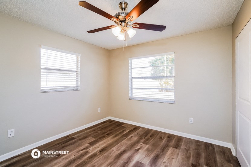 the spacious living room has a ceiling fan and two windows