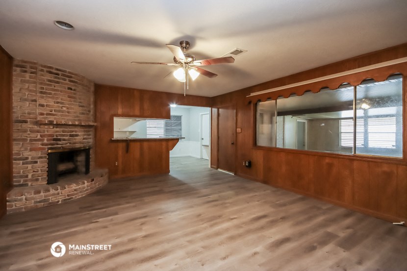 an empty living room with a brick fireplace and a ceiling fan