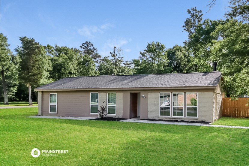 a small tan house with a grassy yard and trees